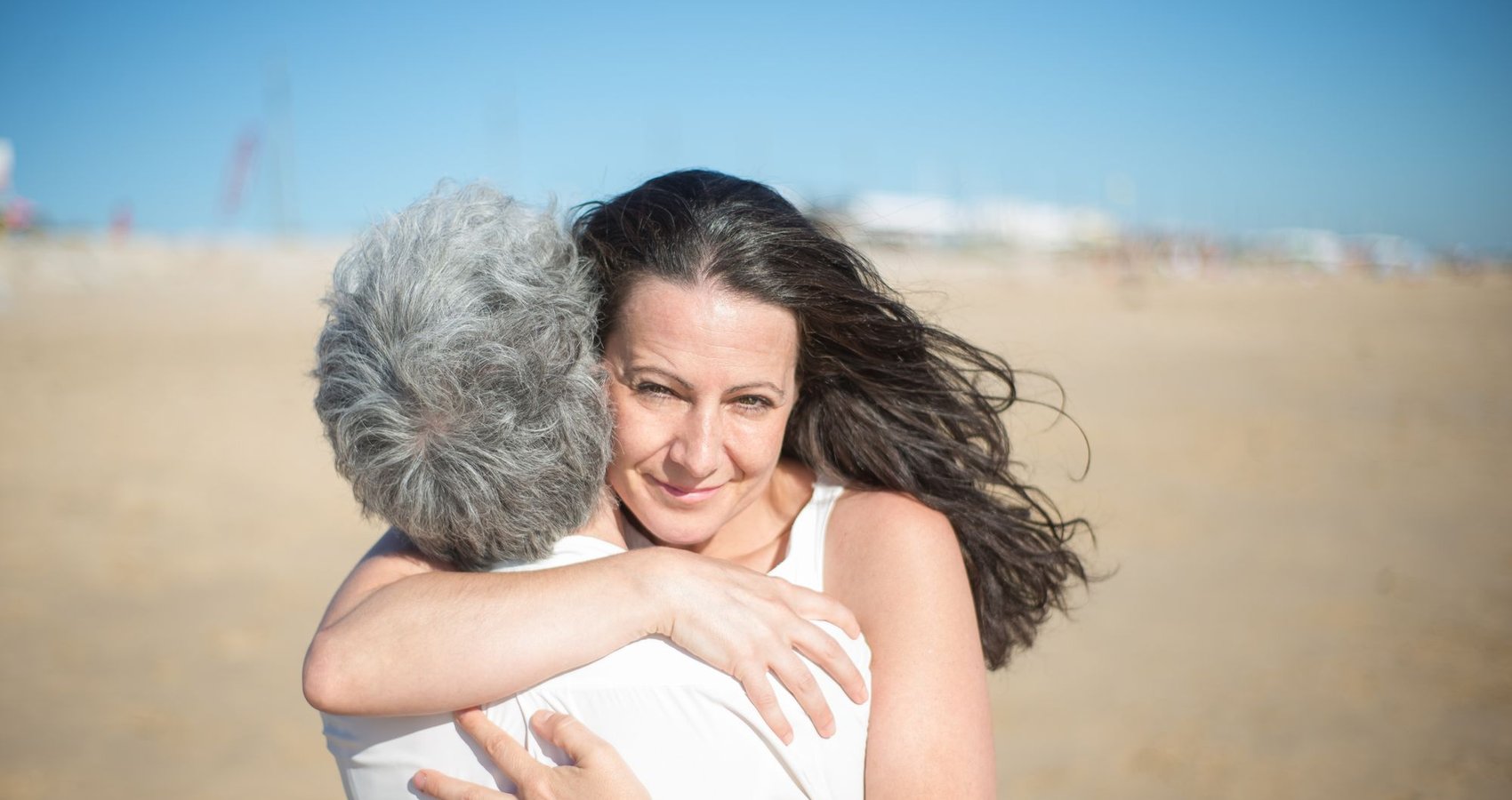 A mother and her adult daughter hugging on the beach